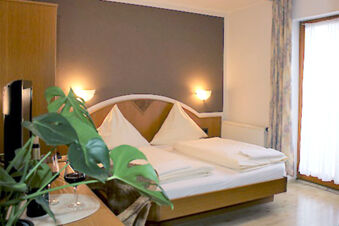 Double bed with white linens in a room at Winzerhotel Weingut Kinges-Kessel featuring a dark accent wall and a glass door with curtains