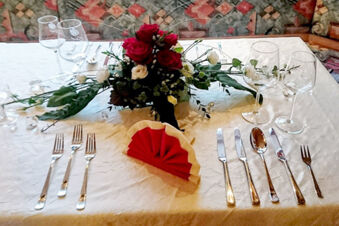 Table setting with three forks, four knives, a spoon, five wine glasses, a red and white folded napkin, and floral centerpiece at Winzerhotel Weingut Kinges-Kessel