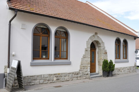 White building with a tiled roof, wooden arched windows, stone doorway, and two potted plants outside Winzerhotel Weingut Kinges-Kessel