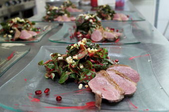 Glass plates with a green leafy salad topped with crumbled cheese and pomegranate seeds served with sliced cooked meat at Winzerhotel Weingut Kinges-Kessel