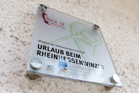 Transparent wall plaque with the text Urlaub beim Rheinhessenwinzer and logos attached to a textured wall at Winzerhotel Weingut Kinges-Kessel