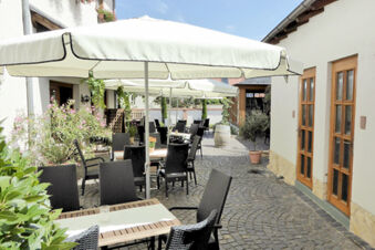 Outdoor dining area with black chairs, wooden tables, white umbrellas, and plants at Winzerhotel Weingut Kinges-Kessel