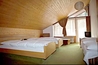 Bedroom with three beds, wooden slanted ceiling, large windows with curtains, green carpet, and TV at Landgasthof Hirsch Dapfen