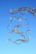 Ornate metal sign featuring a leaping stag surrounded by decorative vines against a clear blue sky at Landgasthof Hirsch Dapfen