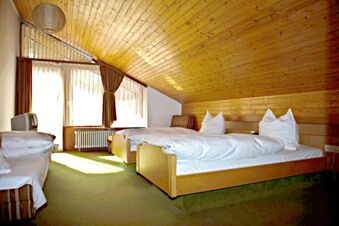 Double bed with white linens under a wood-paneled sloped ceiling in a bright room at Landgasthof Hirsch Dapfen