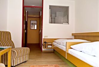 Simple hotel room at Landgasthof Hirsch Dapfen with two single beds, striped armchair, and wooden floor visible