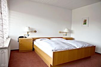 a simple hotel room at Landgasthof Hirsch Dapfen with a wooden double bed white bedding two nightstands with lamps and a phone