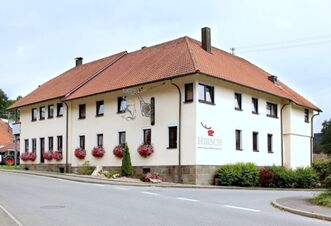 Two-story cream building with red tile roof and flower boxes under windows at Landgasthof Hirsch Dapfen