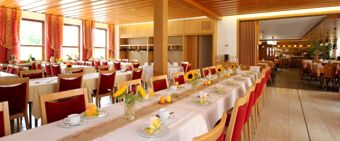 Spacious dining room at Landgasthof Hirsch Dapfen with long tables set with white tablecloths, red chairs and sunflower centerpieces