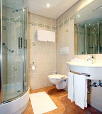 Bathroom of Landgasthof Hirsch Dapfen featuring a glass shower, wall-mounted toilet, sink, towels, and tiled walls and floor