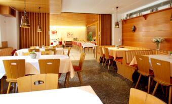 Dining area with wooden chairs and tables covered with white and beige tablecloths inside Landgasthof Hirsch Dapfen