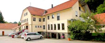 Yellow multi-story building with red tiled roofing and cars parked outside at Landgasthof Hirsch Dapfen surrounded by greenery