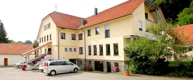 Yellow multi-story building with red tiled roofing and cars parked outside at Landgasthof Hirsch Dapfen surrounded by greenery