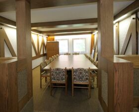 Meeting room with a long table, floral upholstered chairs, large window, and wooden panel walls at Landgasthof Hirsch Dapfen