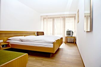 A simple hotel room at Landgasthof Hirsch Dapfen with a double bed, wooden furniture, a small TV, and sheer curtains on the window