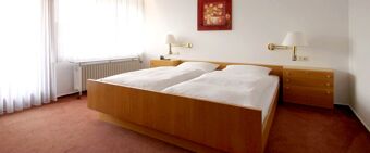 A hotel room at Landgasthof Hirsch Dapfen featuring a wooden double bed with white bedding, two bedside tables, and wall lamps