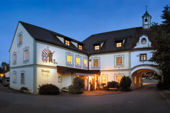 Au&szlig;enansicht des historisch gestalteten Geb&auml;udes von Hotel Restaurant Klosterhof GmbH bei Abendd&auml;mmerung mit beleuchteten Fenstern und Torbogen.