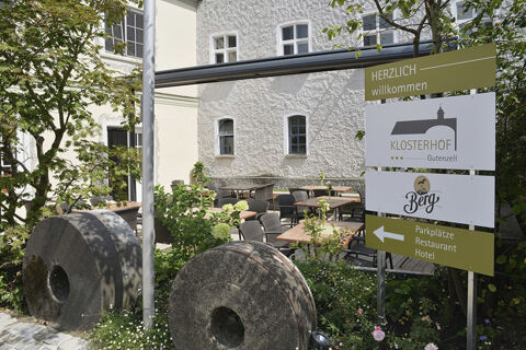 Au&szlig;enbereich des Hotel Restaurant Klosterhof GmbH mit Sitzgelegenheiten, begr&uuml;nten Pflanzungen und einem Schild mit Wegweisern zum Hotel und Restaurant.