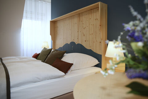 Hell eingerichtetes G&auml;stezimmer mit Holzkopfteil, mehreren Kissen und Lampen im Hotel Restaurant Klosterhof GmbH.