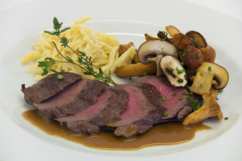 Ein Teller mit rosa gebratenem Fleisch, Pilzen und Sp&auml;tzle, angerichtet im Hotel Restaurant Klosterhof GmbH.