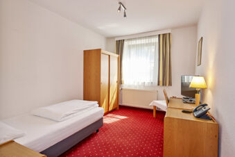 A simple hotel room with a single bed, wooden wardrobe, desk with lamp and phone, and window with curtains at Lodner&acute;s Genie&szlig;erhotel & Hotel Drei Mohren