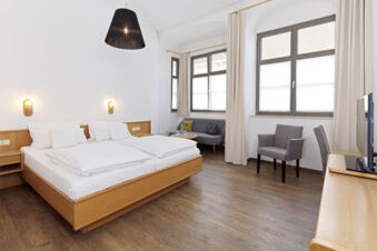 Hotel room at Lodner&acute;s Genie&szlig;erhotel & Hotel Drei Mohren with wooden flooring, a double bed, small sofa, armchair, and TV near large windows