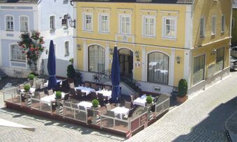 Outdoor dining area with tables, chairs, umbrellas, and plants next to the yellow Lodner&acute;s Genie&szlig;erhotel & Hotel Drei Mohren building