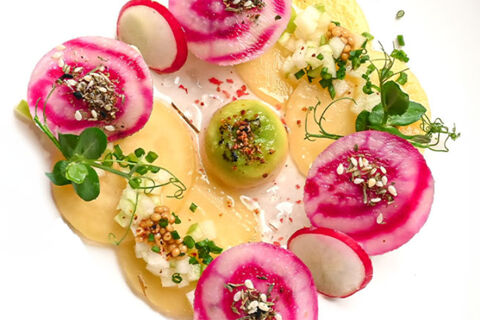 colorful slices of radish and yellow vegetable topped with herbs and seeds presented on a white plate from Lodner&acute;s Genie&szlig;erhotel & Hotel Drei Mohren