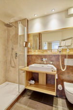 Modern bathroom with glass shower, wooden sink cabinet, wall-mounted hair dryer, and mirror in Lodner&acute;s Genie&szlig;erhotel & Hotel Drei Mohren