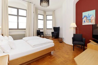 Hotel room at Lodner&acute;s Genie&szlig;erhotel & Hotel Drei Mohren with wooden flooring, a double bed, black chairs, and a red accent wall with artwork