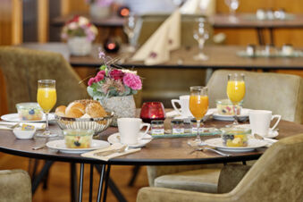 Table set with glasses of orange juice, coffee cups, fruit bowls, bread rolls, and a flower centerpiece at Lodner&acute;s Genie&szlig;erhotel & Hotel Drei Mohren