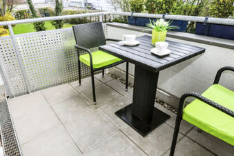 Piccolo balcone con due sedie e tavolo con cuscini verdi e una pianta nell'Hotel Garni Metzingen, dotato di tazze.