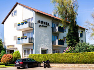 Facciata dell'Hotel Garni Metzingen con balconi, piante e parcheggio nei dintorni soleggiati.