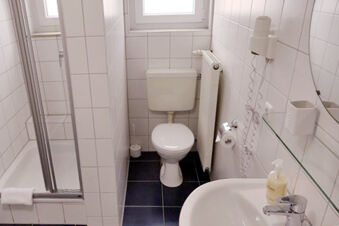 Bagno pulito e compatto con WC, doccia e lavabo nell'Hotel Garni Metzingen con piastrelle bianche.