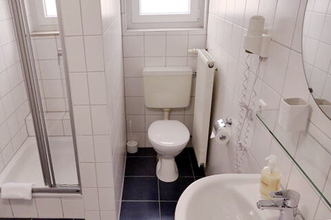 Čist&aacute; a kompaktn&aacute; k&uacute;peľňa s WC, sprchovac&iacute;m k&uacute;tom a um&yacute;vadlom v hoteli Garni Metzingen s bielymi obkladačkami.