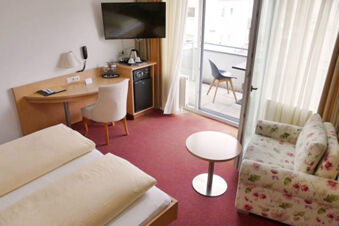 Luminosa camera dell'Hotel Garni Metzingen con due letti, scrivania, piccolo balcone e divano a fiori.