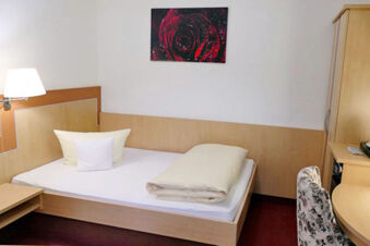 Luminosa camera d'albergo con letto singolo, scrivania e sedia a motivi floreali dell'Hotel Garni Metzingen, arredata in modo semplice e invitante.