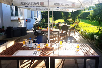 Terrazza soleggiata dell'Hotel Garni Metzingen con tavoli, sedie e ombrelloni in legno in un'area verde del giardino.