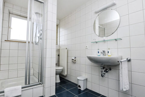 Svetl&aacute; k&uacute;peľňa s vaňou, sprchovac&iacute;m k&uacute;tom, WC a um&yacute;vadlom v hoteli Garni Metzingen, čist&aacute; a funkčne navrhnut&aacute;.