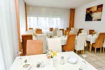 Ristorante luminoso e accogliente con sedie bianche e arancioni nell'Hotel Garni Metzingen, tavoli apparecchiati e decorazioni.