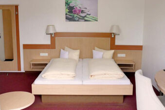 Camera d'albergo arredata in modo luminoso con letto matrimoniale, comodini e area salotto dell'Hotel Garni Metzingen, accogliente e funzionale.