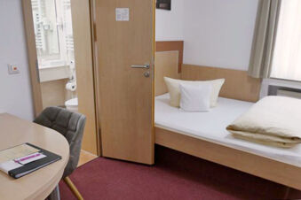 Luminosa camera singola con mobili in legno, letto e scrivania dell'Hotel Garni Metzingen, con vista sul bagno adiacente.