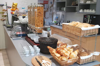 Colazione a buffet con vari panini, croissant, cereali e tazze disposti in un lungo bancone dell'Hotel Garni Metzingen.