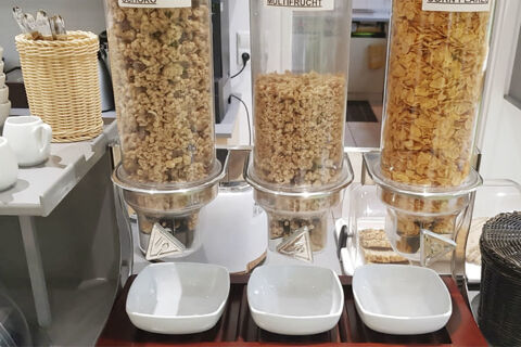 Pohľad na raňajkov&eacute; menu s tromi d&aacute;vkovačmi na čokol&aacute;du, ovocie a kukuričn&eacute; lupienky v hoteli Garni Metzingen.