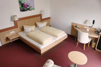 Camera doppia dell'Hotel Garni Metzingen arredata in modo luminoso con due letti singoli, scrivania, sedia e un piccolo tavolo rotondo.