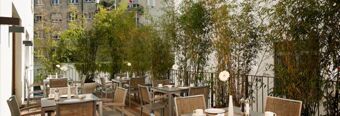 Outdoor dining area with tables, chairs, white cups, plates, and tall green plants at NH Hotel Frankfurt Messe