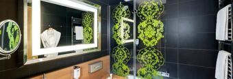 Bathroom interior at NH Hotel Frankfurt Messe with backlit mirror, glass shower door with green floral patterns, and white towels