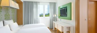 Hotel room at NH Hotel Frankfurt Messe with a double bed, green patterned wallpaper, wall-mounted TV, and window curtains