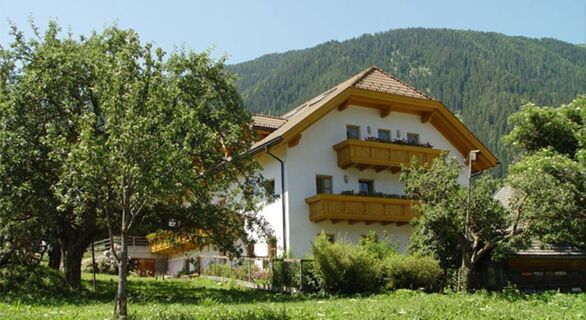 Ваканционните апартаменти във фермата Lexmairhof се отличават с традиционна бяла сграда с дървени балкони, заобиколена от дървета и планини в провинцията.
