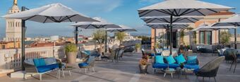 Outdoor terrace seating with umbrellas, blue cushions, potted plants, and city view at NH Collection Roma Palazzo Cinquecento